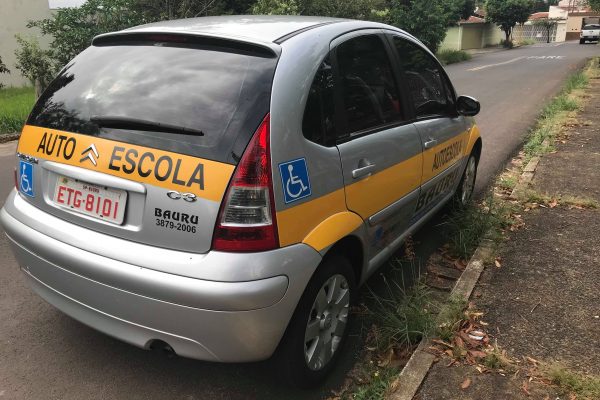 Imagem de um carro adaptado de autoescola estacionado em uma rua. Carteira especial